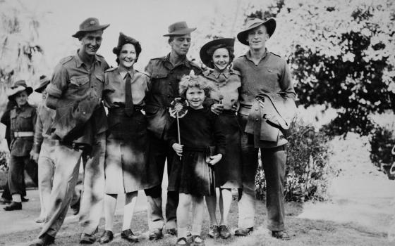 A group of soldiers, three men and two women in the Brisbane Botanic Gardens. They are joined by a young girl. Other soldiers walk past in the background. The figures are in uniform. The young girl holds a windmill fan.