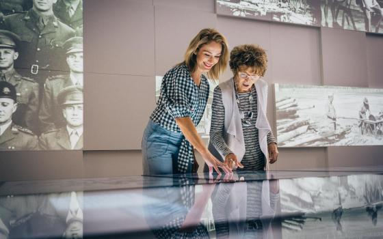 Two happy looking women using touchscreens. Projections are shown on the wall behind them with old photographs.