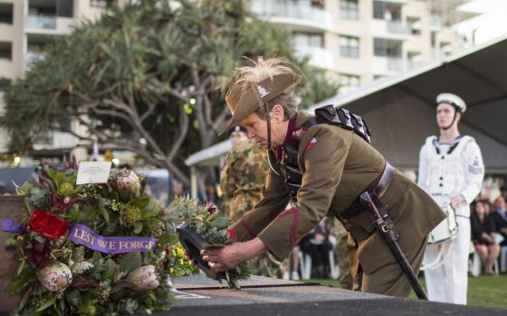 Man wearing military uniform laying a wreath of flowers on a memorial.