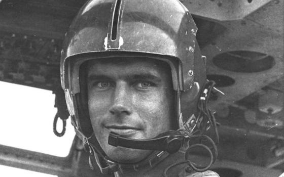 Black and white photograph of a mean wearing a flight helmet in a plane.