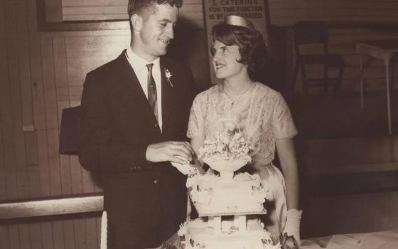 Old photograph of pride and groom looking at each other. A wedding cake is in front of them.