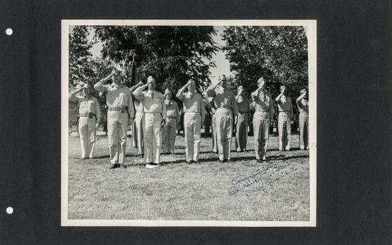 Old black and white photograph of soldiers saluting pasted onto black card.