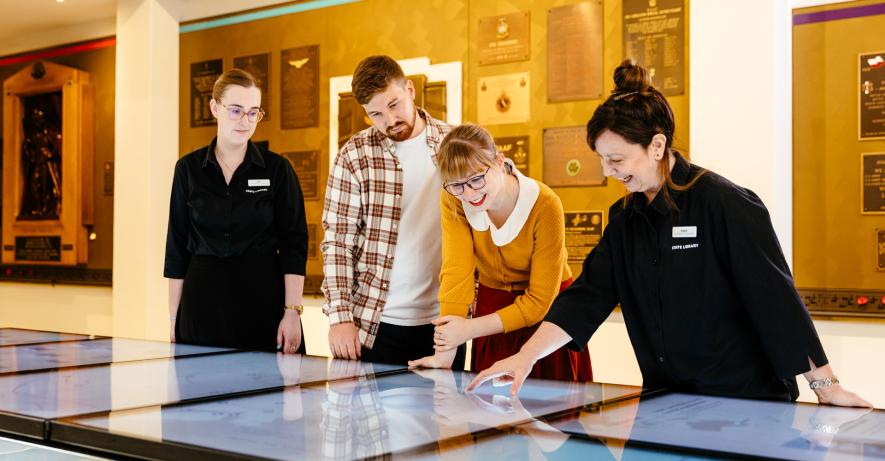 Two visitors use the interactive screens in the gallery with two staff members.