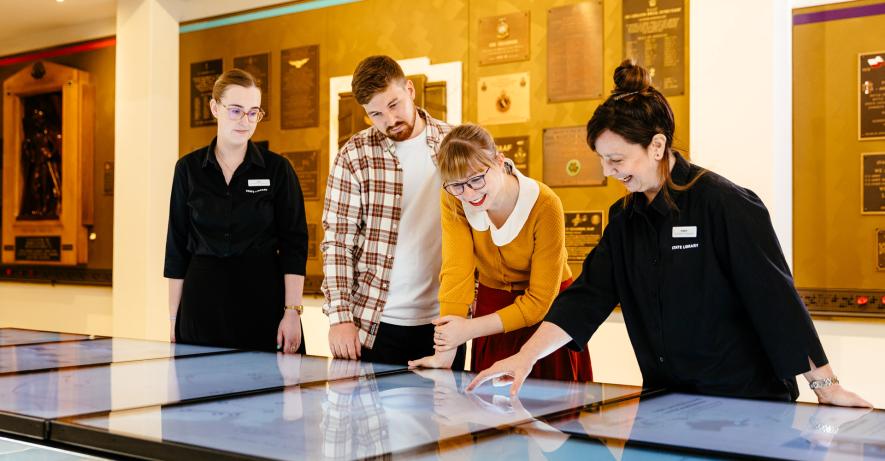 Two visitors use the interactive screens in the gallery with two staff members. 