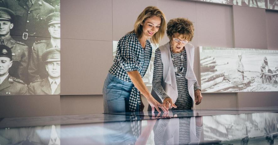 Two happy looking women using touchscreens. Projections are shown on the wall behind them with old photographs.