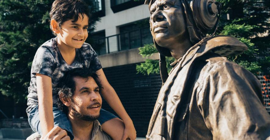 Father with a child on his shoulders looking up at a statue outside.