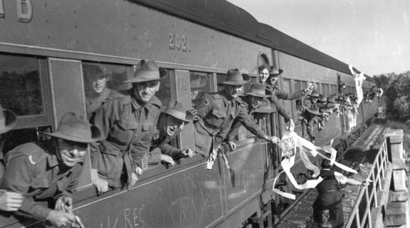 Black and white photograph of soldiers leaning out of train carriage windows.