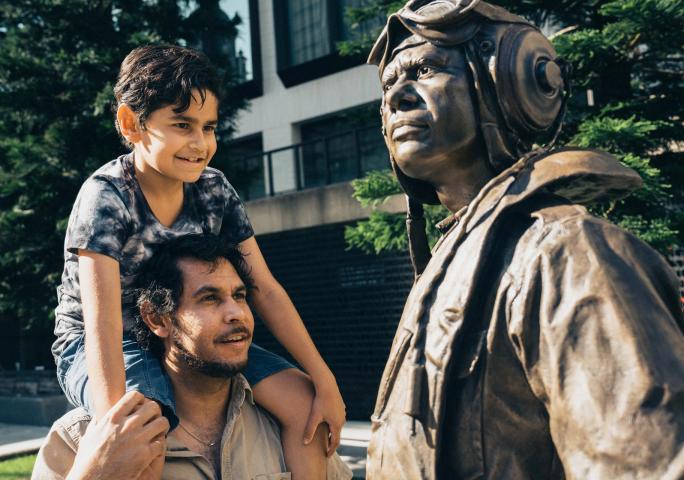 Father with a child on his shoulders looking up at a statue outside.