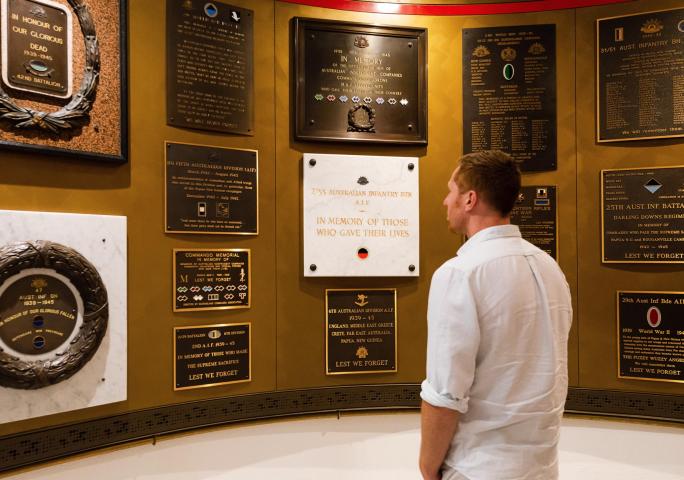 Man looking at memorial plaques on a gold, curved wall.