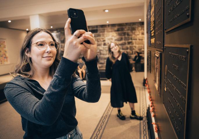 Woman taking a photo of a memorial plaque with her phone.