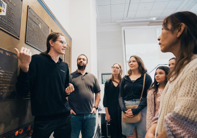 A group of people facing a staff member who is gesturing towards a plaque.